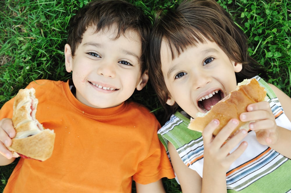 Two cute boys laying on ground in nature and happily eating healthy food