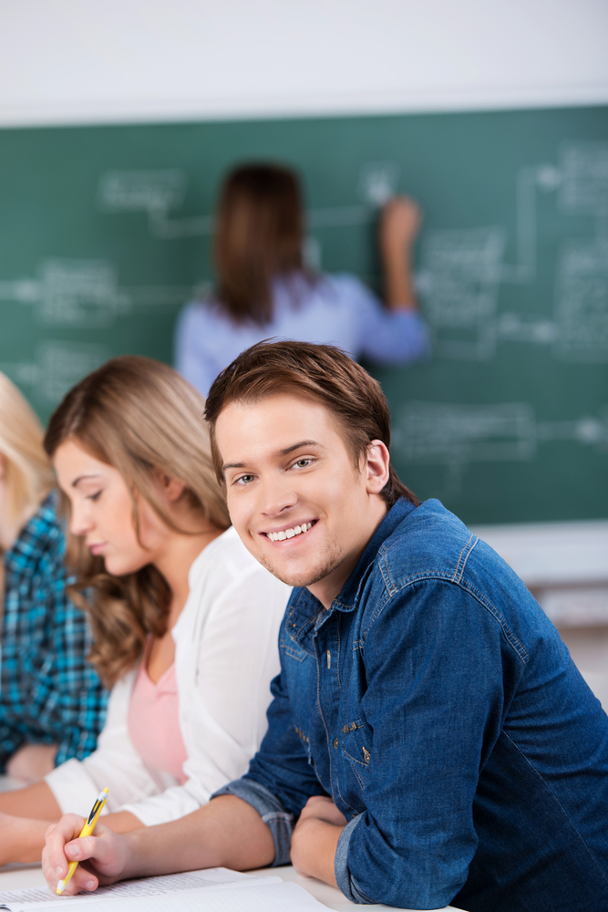 Portrait of young male student sitting with female classmates and teacher at desk