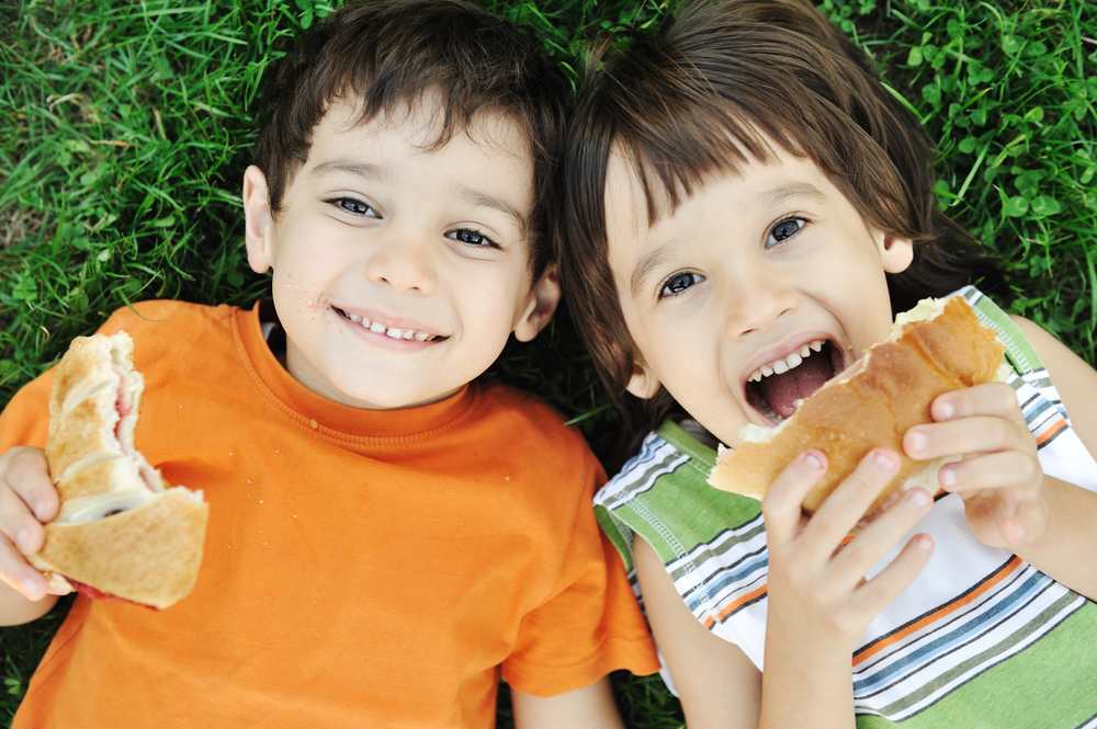 Two cute boys laying on ground in nature and happily eating healthy food
